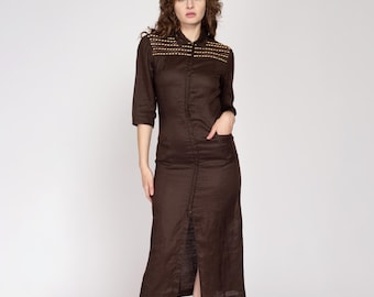 May include: A brown linen dress with a button-up front and a long, flowing skirt. The dress has a collar and a pocket on the left side. The dress is decorated with gold-colored beads on the shoulders.