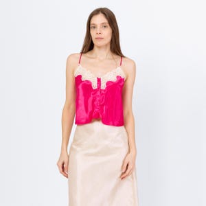 May include: A hot pink satin camisole with spaghetti straps and a cream-colored lace trim. The camisole has a button-up front and is paired with a beige satin skirt. The outfit is displayed against a white background.
