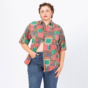 May include: Short-sleeved button-up shirt with a patchwork design in red, green, and blue. The shirt features a collared neckline and is paired with blue jeans. The overall style is casual and vintage.