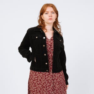 May include: A black corduroy jacket with silver buttons and pockets. The jacket is worn over a red floral print dress. The outfit is set against a white background.