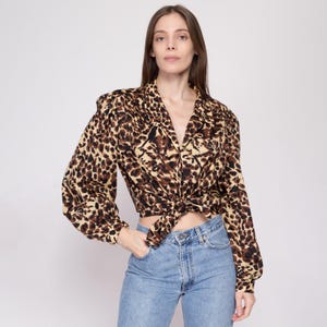May include: A long-sleeved, brown and beige leopard print blouse with a V-neck and a knotted front. The blouse has a relaxed fit and is made of a soft, silky fabric.