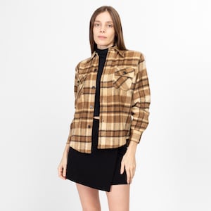 May include: A brown and beige plaid flannel shirt with long sleeves and a button-up front. The shirt has two chest pockets and a black mock neck shirt underneath.