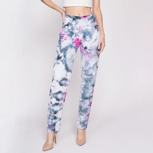 May include: A pair of blue jeans with a white and pink tie-dye pattern. The jeans have a straight leg and a high waist.