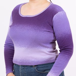 May include: A long-sleeved shirt with a purple ombre design. The shirt has a scoop neck and is made of a soft, stretchy fabric.