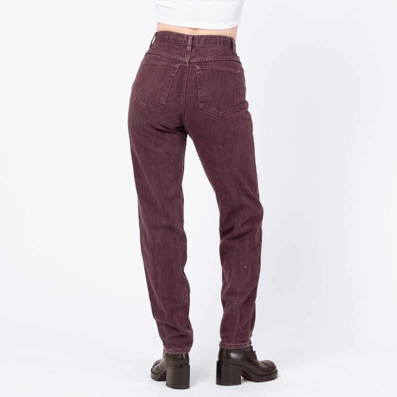 May include: A pair of high-waisted, dark burgundy jeans. The jeans have a classic five-pocket design and a straight leg fit. The model is wearing black heeled boots. The background is plain white.