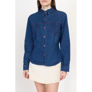 May include: A blue denim shirt with long sleeves and a button-up front. The shirt has red stitching around the pockets and collar.