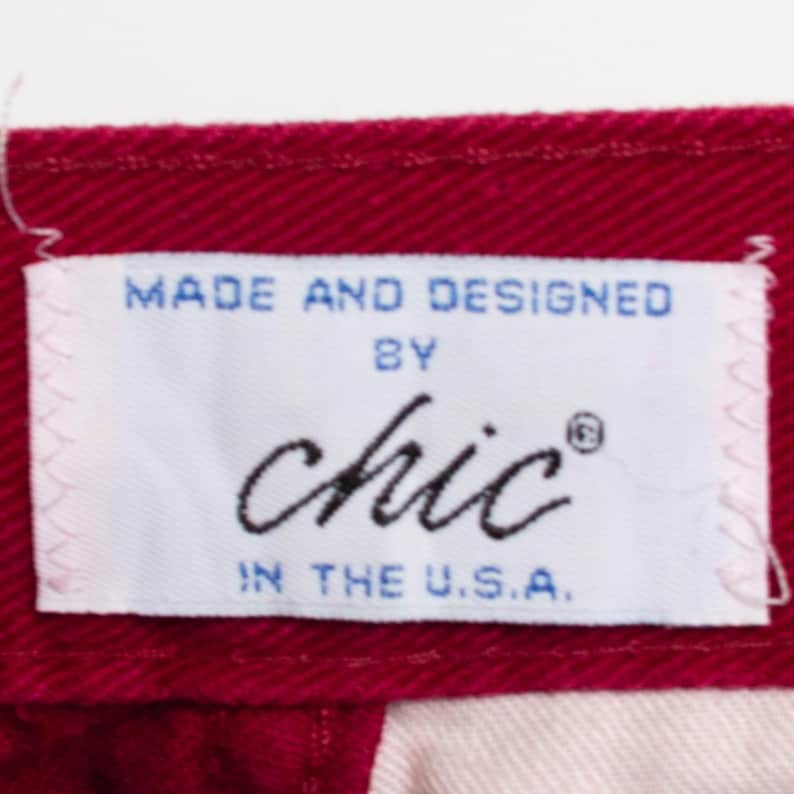 May include: A white label with blue text that reads "Made and Designed by Chic&reg; in the U.S.A." The label is sewn onto a burgundy fabric.
