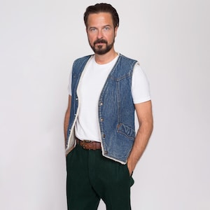 Può includere: Un uomo indossa un giubbotto di jeans blu con fodera in sherpa bianca, una t-shirt bianca, una cintura in pelle marrone e pantaloni verde scuro.