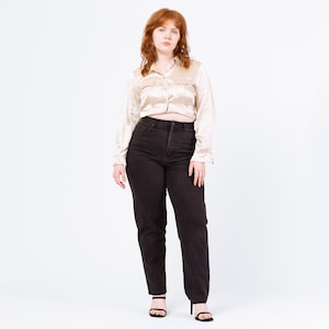 Peut inclure: Une personne porte une chemise boutonnée en satin beige avec deux poches de poitrine et un jean en denim délavé foncé. Le jean est taille haute et à jambes droites. Elle porte des sandales noires.