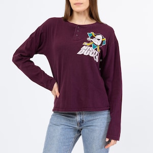Puede incluir: Una camiseta de manga larga de color burdeos con un gráfico de un pato de dibujos animados con una máscara de hockey y el texto "Mighty Ducks".