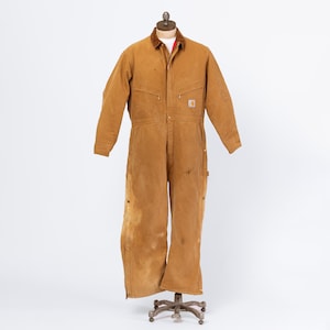 May include: A brown Carhartt work jumpsuit with a brown corduroy collar and a red lining peeking through. The jumpsuit has multiple pockets, a zipper closure, and is displayed on a mannequin. The garment shows signs of wear and tear.