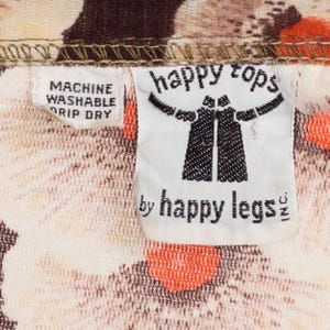 May include: White fabric with a brown and orange floral pattern. A white tag with black text reads "happy tops by happy legs". A smaller white tag with black text reads "machine washable drip dry".