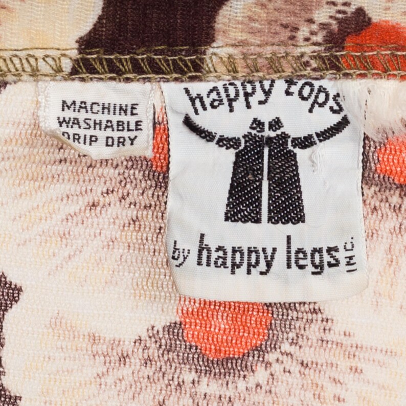 May include: White fabric with a brown and orange floral pattern. A white tag with black text reads "happy tops by happy legs". A smaller white tag with black text reads "machine washable drip dry".