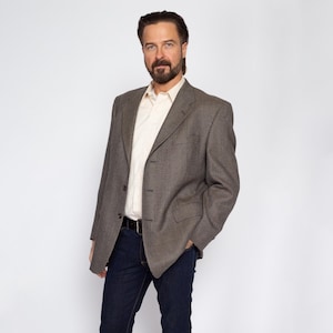 May include: A brown and black checkered blazer with a single button closure. The blazer has a white collared shirt underneath and a brown leather belt.