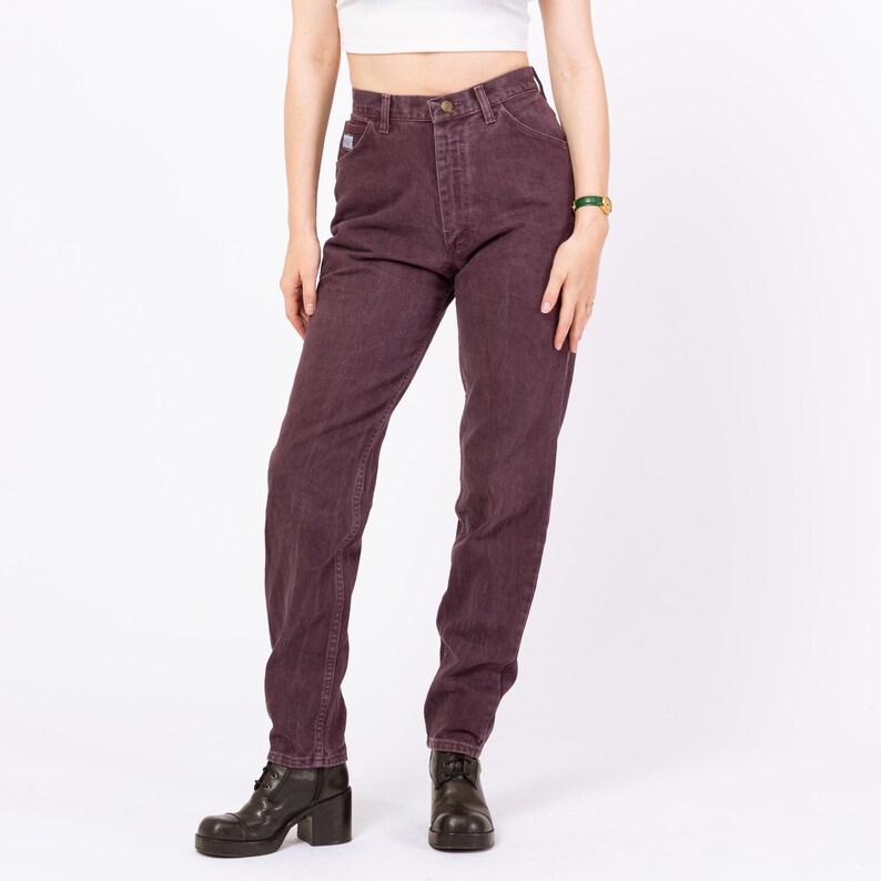 May include: Dark purple denim jeans with a classic five-pocket design. The jeans have a high waist and a straight leg fit. The model is wearing black boots. The jeans are made of a durable denim material.