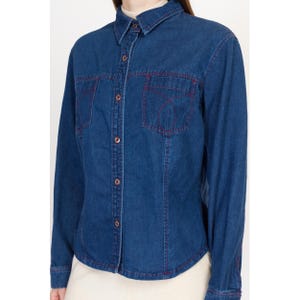 May include: A blue denim shirt with long sleeves and a button-up front. The shirt has red stitching around the pockets and collar.