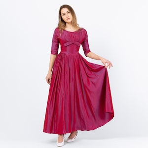 Könnte beinhalten: Ein magentafarbenes, langes Satin-Kleid mit einem taillierten Oberteil und einem weiten Rock. Das Kleid hat eine Schleife an der Taille und Dreiviertelärmel.