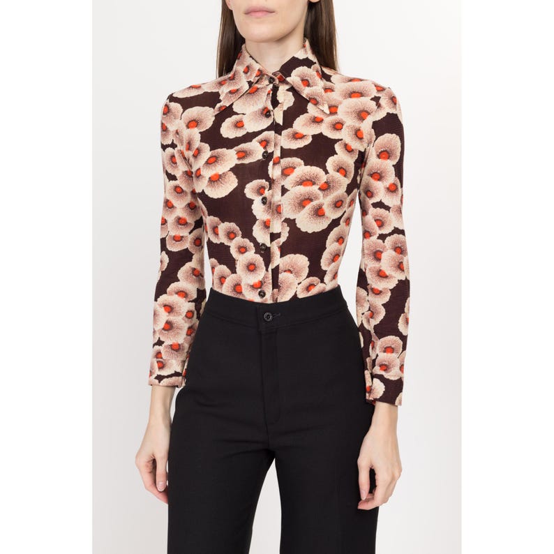 May include: A brown long-sleeved shirt with a white and orange floral print. The shirt has a collar and button closure.