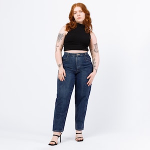 Puede incluir: Una persona con una camiseta negra de cuello alto y pantalones vaqueros azules. La persona tiene el pelo rojo y tatuajes en los brazos.