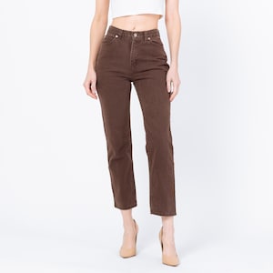 May include: Brown high-waisted jeans with a straight leg. The jeans have a classic five-pocket design and a button and zipper closure. The model is wearing nude-colored heels.