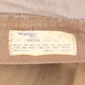 May include: A brown Wrangler brand clothing label with white text. The label states "STYLE 13MWZKH", "WAIST 30", "LENGTH 30", "MACHINE WASH WITH LIKE COLORS ONLY NON-CHLORINE BLEACH WHEN NEEDED TUMBLE DRY REMOVE PROMPTLY", "MADE IN USA", "C 8BAF666 2 WPL6428".