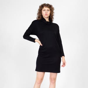 May include: A black long-sleeved dress with a mock neck and a slightly loose fit. The dress has a simple design and is made of a soft, comfortable fabric.