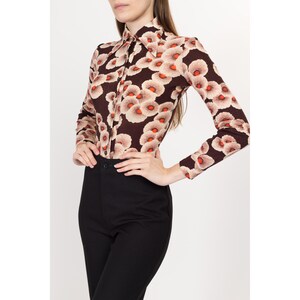May include: A brown long-sleeved shirt with a floral print featuring white and orange flowers.