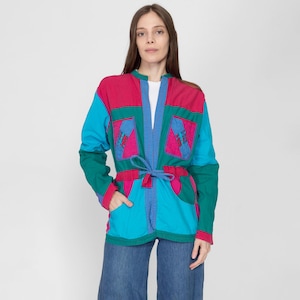 Könnte beinhalten: Eine bunte Patchworkjacke mit einem Bindegürtel. Die Jacke besteht aus verschiedenen Blautönen, Rosa und Grün. Die Jacke hat einen Kragen und lange Ärmel.