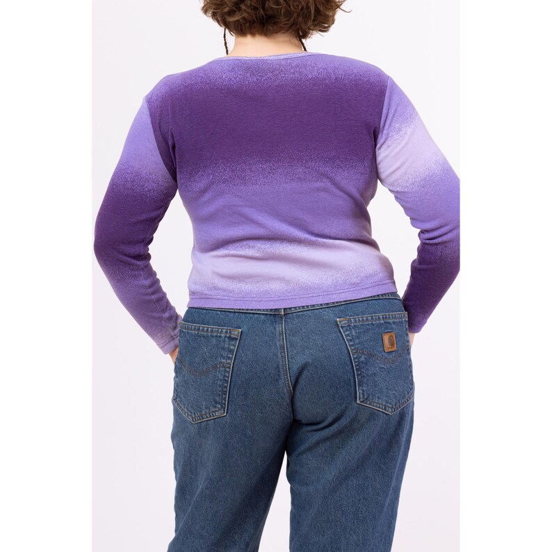 May include: A long-sleeved, purple ombre sweater with a V-neck. The sweater is made of a soft, knit fabric and has a relaxed fit.