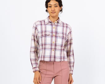 Puede incluir: Una camisa de manga larga a cuadros blancos y rosas con cierre de botones y dos bolsillos en el pecho. La camisa es corta y tiene un corte holgado.