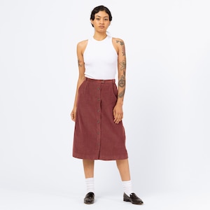 May include: A maroon corduroy midi skirt with a button front closure. The skirt has a relaxed fit and falls to the mid-calf.