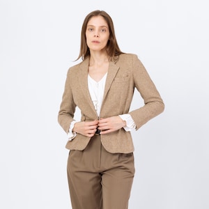 Puede incluir: Una blazer marrón claro con estampado de pata de gallo y solapa con muescas, combinada con pantalones marrones y una blusa blanca. La blazer presenta un diseño clásico con cierre de dos botones. El atuendo es adecuado para negocios o informal.