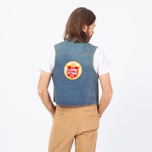 May include: A denim vest with a Lone Star Beer patch. The patch is circular with a red and white design and the words "Lone Star Beer". The vest is a light blue color and has a classic denim design.
