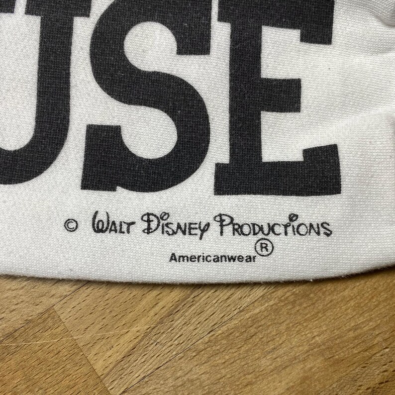 May include: White t-shirt with the word "MOUSE" printed in black. The shirt has a copyright notice for Walt Disney Productions and the Americanwear logo.