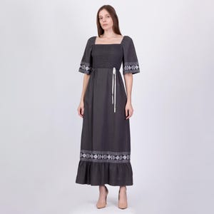 May include: A gray maxi dress with a square neckline and white embroidered details. The dress has a smocked bodice and a ruffled hem.