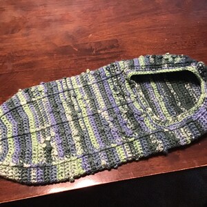 May include: A crocheted slipper in shades of green, blue, and purple. The slipper has a textured, striped pattern and a rounded toe.