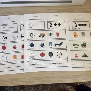 May include: Educational worksheets with the letters A, B, and numbers 1, 2, and 3. Each sheet features illustrations of objects like an airplane, a bus, a cat, and a calculator, along with shapes and colors.