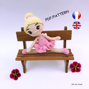 Może przedstawiać: Dziewczynka-balerina wykonana na szydełku z blond włosami i różową spódniczką, siedząca w szpagacie na drewnianej ławce. Lalka ma na sobie różowe baletki. Obraz zawiera tekst "PDF/PATTERN" oraz flagi Francji i Wielkiej Brytanii.