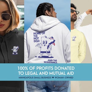 Puede incluir: Variedad de prendas con un gráfico de dibujos animados de un plato con una cara, sosteniendo una bandera y una cuchara. El texto "HOME OF THE HOT DISH AND THE RESISTANCE" se muestra en la parte posterior de una sudadera con capucha blanca y una camiseta de manga larga. Una sudadera con capucha negra también presenta el gráfico.
