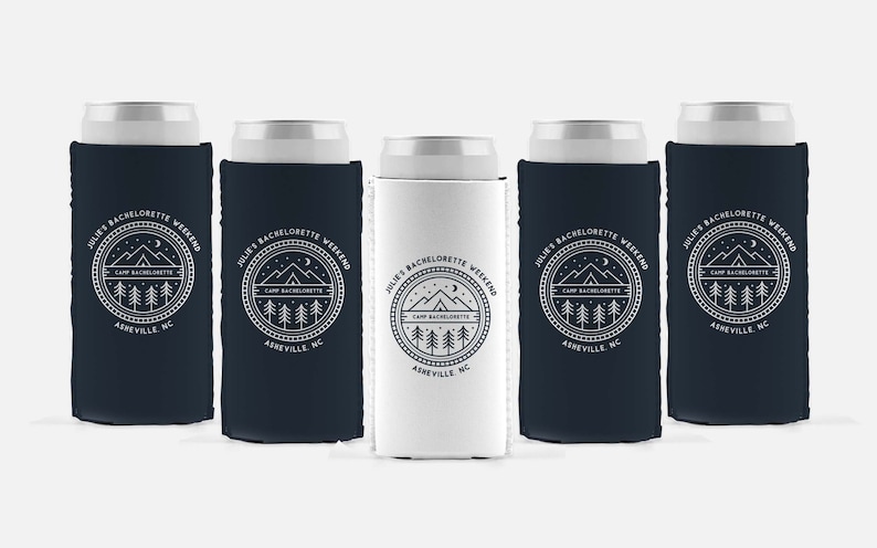 May include: Five white and navy blue can coolers with a white graphic design. The design features a mountain range, a crescent moon, a tent, and trees. The text reads "Julie's Bachelorette Weekend Camp Bachelorette Asheville, NC".