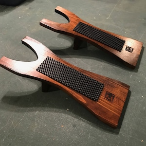 May include: Two wooden boot jacks with black rubber inserts. The boot jacks are stained a dark brown color and have a small logo on the side.