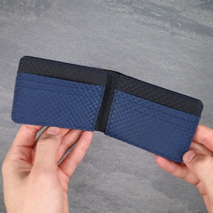 May include: A bifold wallet featuring a blue and black grid pattern on the exterior and interior card slots. The wallet is constructed with dark blue textured material and black accents, showcasing multiple horizontal slots for organizing cards.