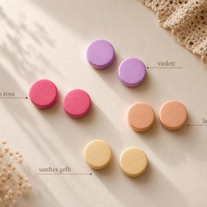 Op de afbeelding: Vier paren ronde knopen in verschillende kleuren, waaronder violet, donkerroze, zalmkleurig en zachtgeel. Elk paar is in een horizontale rij geplaatst. De tekstlabels violett, dunkles rosa, lachsfarben en sanftes gelb wijzen naar elke kleur.