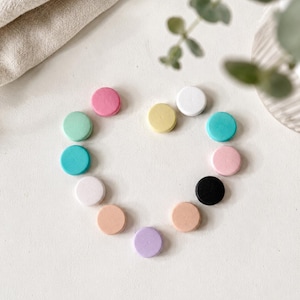 Peut inclure: Une collection de douze petits disques en bois plats et circulaires disposés en forme de cœur. Les disques présentent une variété de couleurs mates unies, notamment rose, vert menthe, bleu sarcelle, blanc, jaune, noir, pêche et lavande.