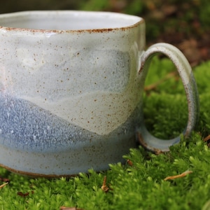 May include: A white ceramic mug with a blue and grey glaze. The mug has a speckled finish and a rounded handle.