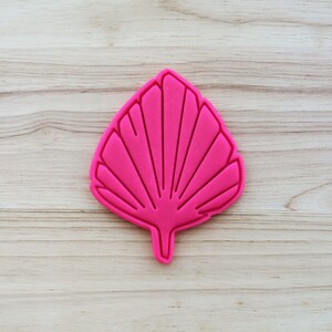 May include: Pink plastic cookie cutter shaped like a large leaf with a fan-like design.