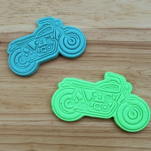 May include: Two plastic cookie cutters shaped like motorcycles. The motorcycle on the left is blue and the motorcycle on the right is green.