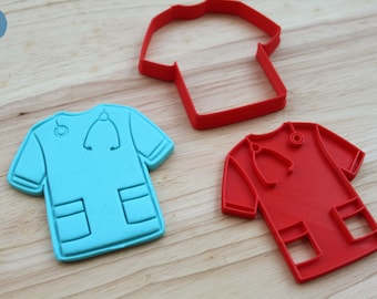 May include: A light blue scrub top cookie cutter with a stethoscope and pocket detail, a red scrub top cookie cutter with a stethoscope and pocket detail, and a red plain t-shirt shaped cookie cutter outline, all featuring PETIT CRAFT text.
