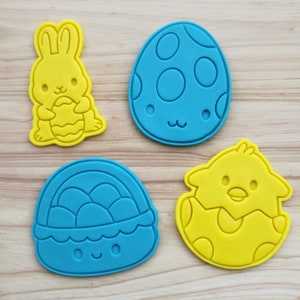 Puede incluir: Cuatro cortadores de galletas con temática de Pascua: un huevo azul con manchas blancas, un pollito amarillo en un huevo, una cesta azul con huevos y un conejito amarillo sosteniendo un huevo.