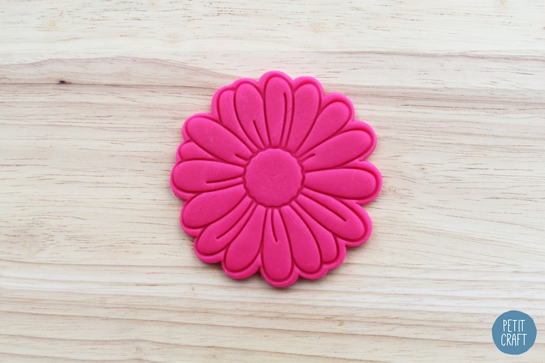 May include: A bright pink cookie cutter shaped like a daisy flower. The cutter has a detailed design with multiple petals.